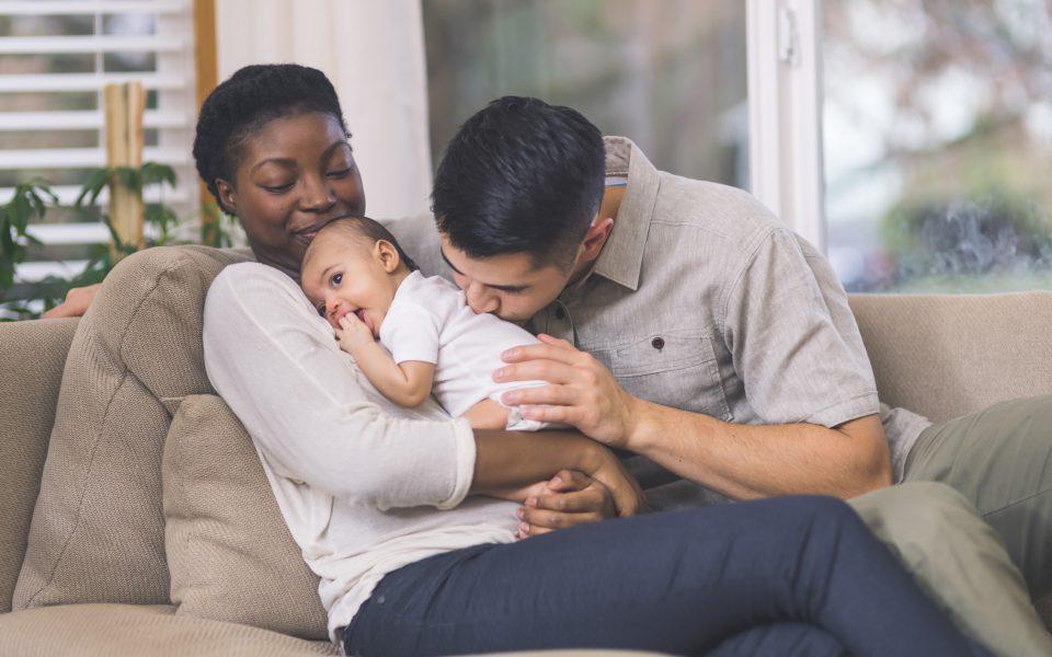 couple snuggle with their infant daughter on the couch in their living room